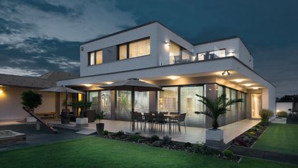 Modernes Haus bei Dämmerung mit Innenbeleuchtung und runtergelassenen Raffstoren