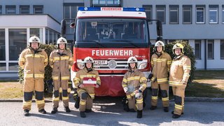 Feuerwehrauto und Mitarbeiter in der Einsatzkleidung vor Verwaltungsgebäude