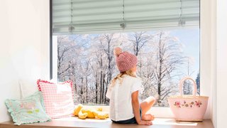 Kind blickt durch Fenster auf Winterlandschaft