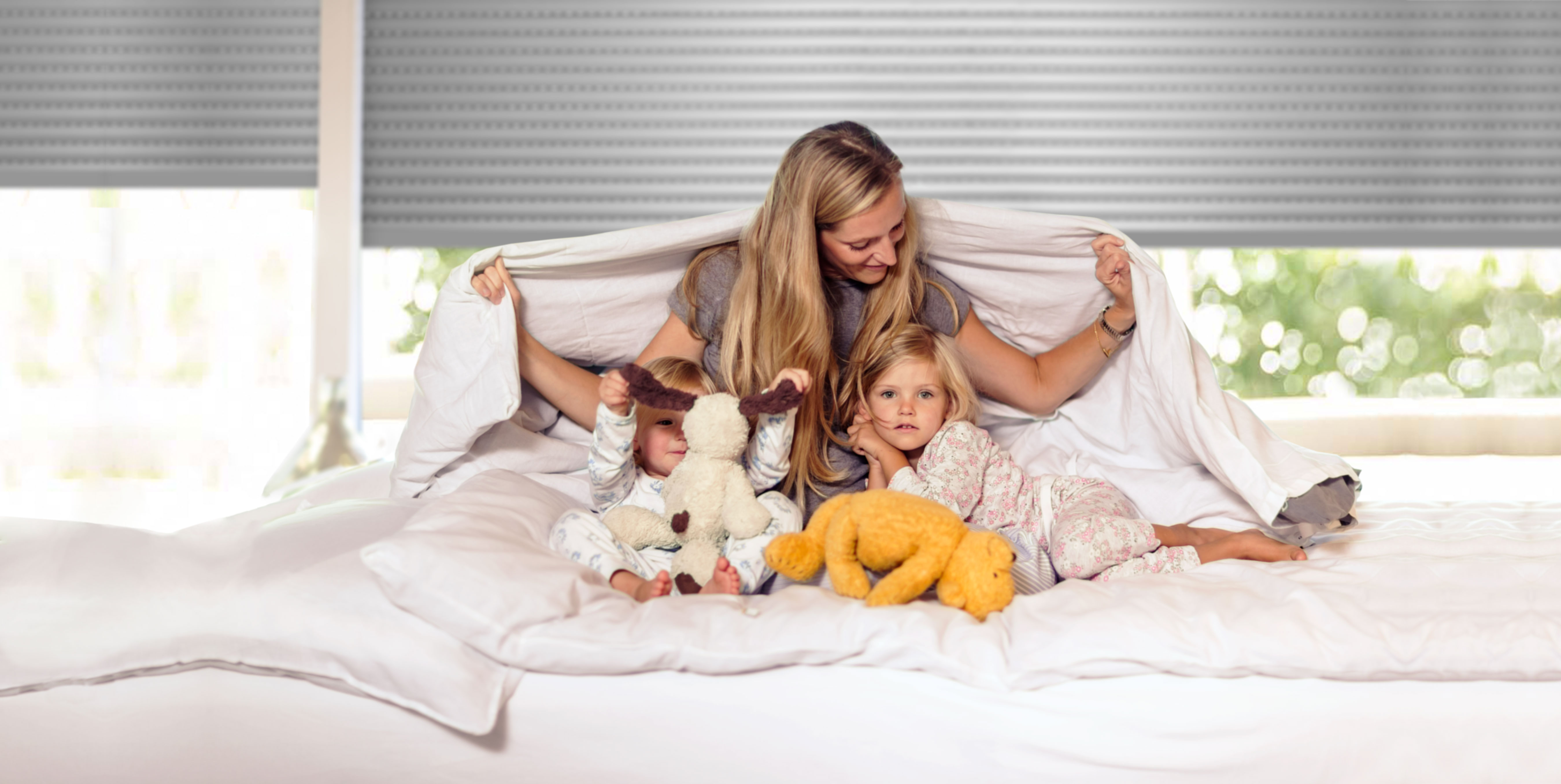 Familie sitzt auf Bett im Schlafzimmer vor Rollladen