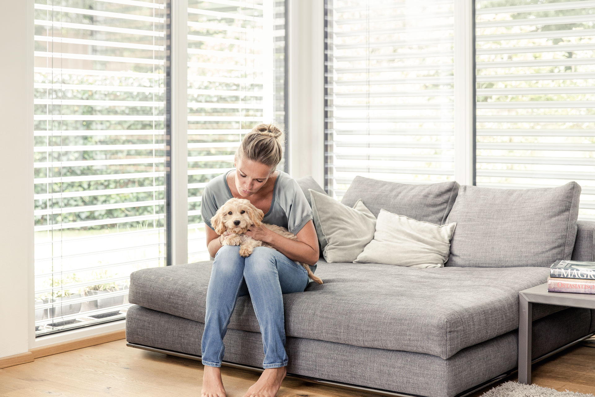 Frau sitzt mit kleinem Hund auf Sofa vor Raffstore