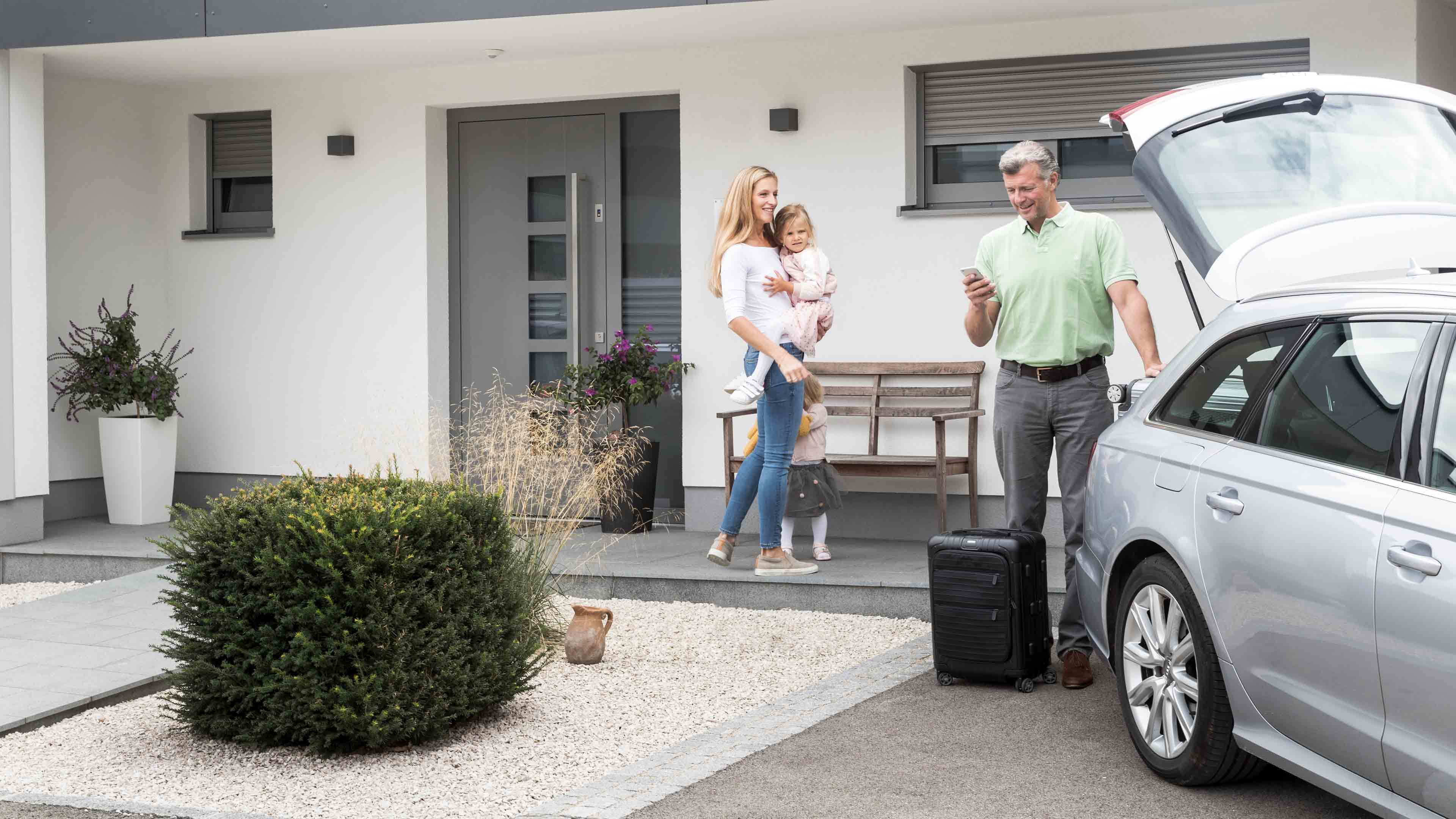 Familie mit Auto vor Haus mit Rollläden