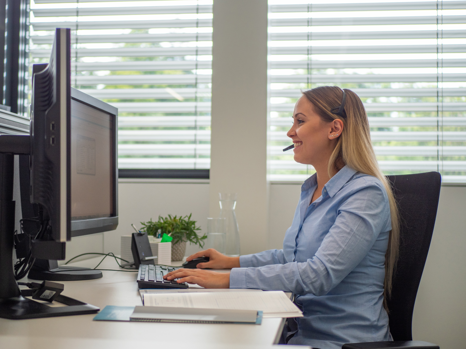 Blonde Frau sitzt am Schreibtisch mit Headset